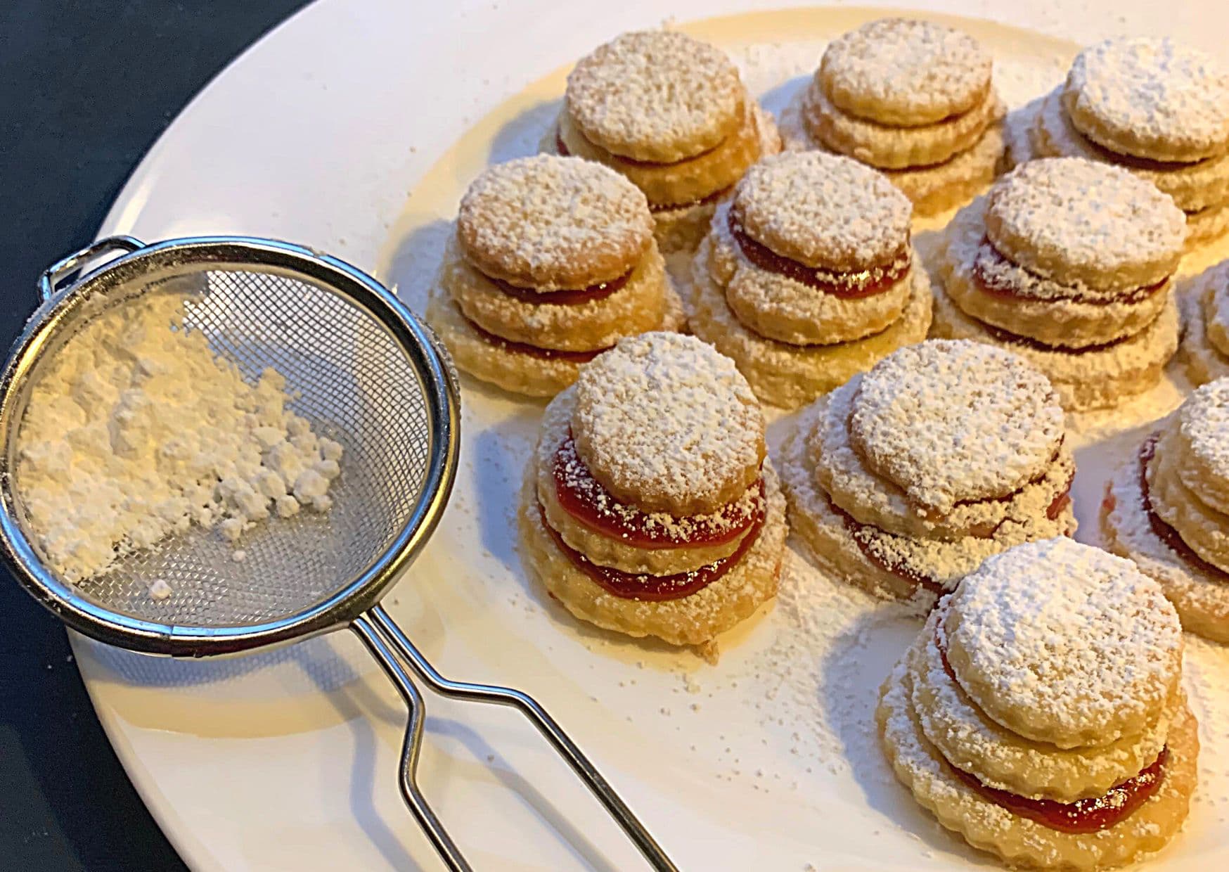German Christmas terraces, on a plate, lightly dusted and ready to eat, with a sieve of powdered sugar on the left.