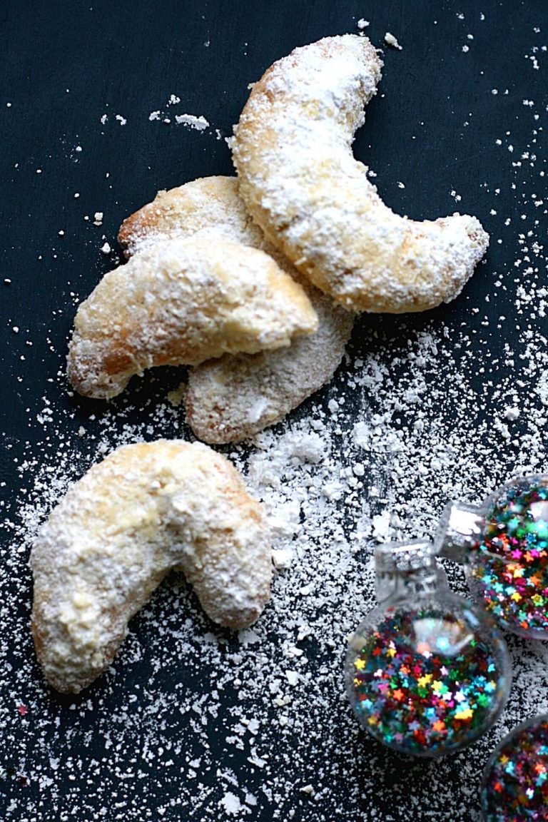 A small pile of vanille Kipferl, or vanilla crescents, with icing sugar and Christmas baubles.