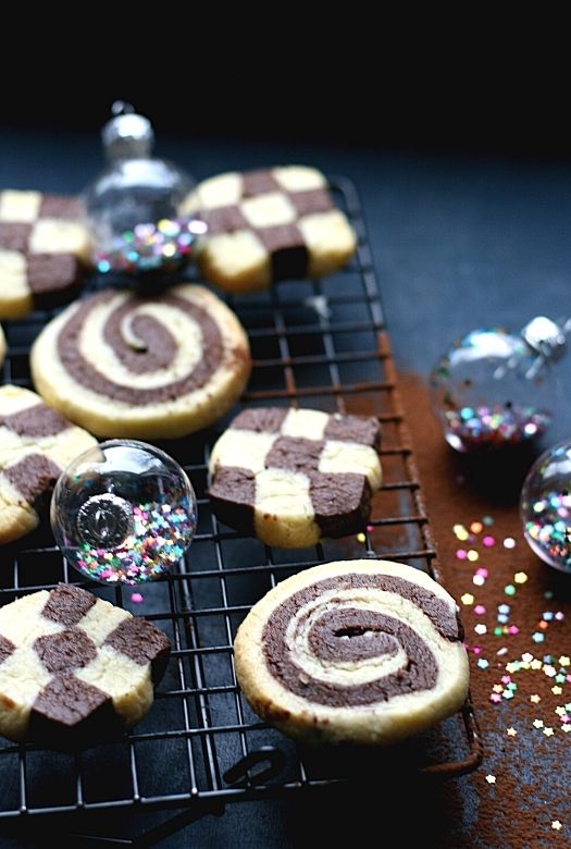 Traditional German black and white cookies in swirl and checkerboard design, on a wire rack. Image also include Christmas baubles with glitter and cocoa powder