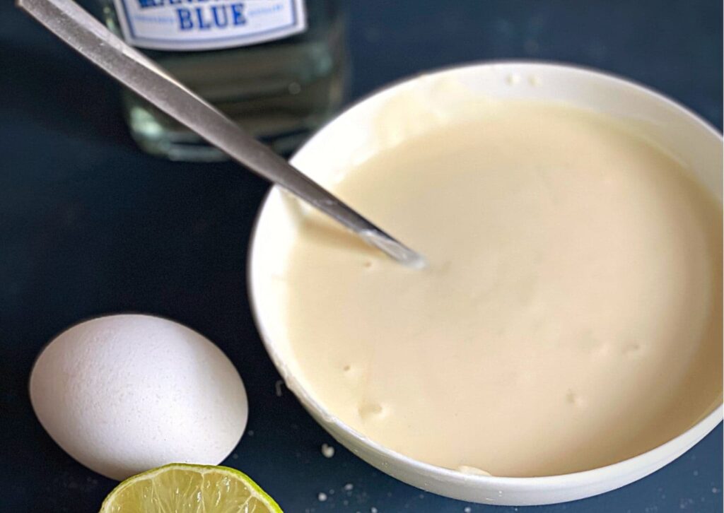 Homemade gin mayonnaise, shown with an egg, half a lime and a bottle of gin
