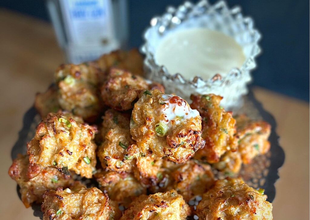 Warm chicken balls with a glass bowl of homemade gin mayonnaise on a silver platter, with a bottle of gin in the background.
